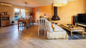 A cozy living room with a wooden floor, a sofa, a coffee table, and a TV. There is a dining area with a table and chairs, and a kitchen area with cabinets and a stove. - Maison Flammarion - Welkeys (Avignon)
