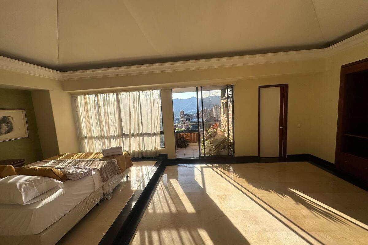 A spacious room with a large bed, a sliding glass door leading to a balcony, and a framed picture on the wall.