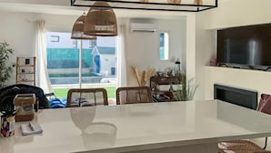 Eine moderne Küche mit einer großen Kochinsel, Korbstühlen und einem an der Wand montierten Fernseher.