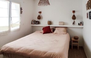 Ein Schlafzimmer mit einem Bett, einem Nachttisch, einem Regal mit Dekoration und einem Fenster.