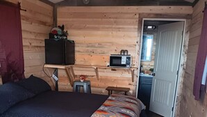 A cozy wooden room with a bed, a small table, a microwave, and a door leading to another room. - Sinopah #5 (East Glacier Park)