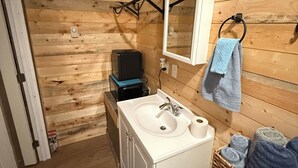 A wooden-paneled bathroom with a sink, mirror, towel rack, and a basket of towels. - Sinopah #5 (East Glacier Park)