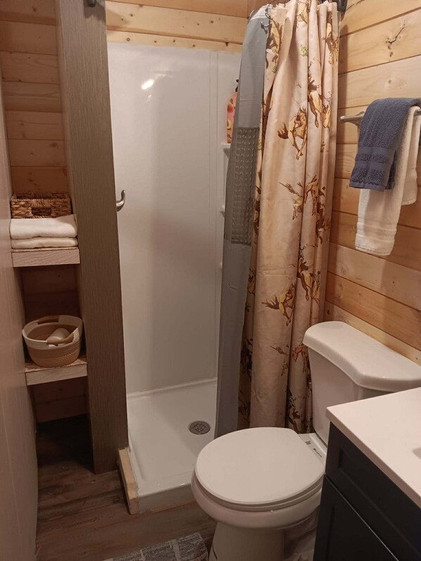 Ein Badezimmer mit Holzwänden, einer Dusche, einer Toilette und einem Ablagefach mit Handtüchern.