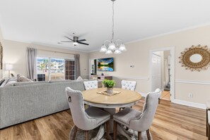 Un coin repas avec une table ronde, quatre chaises, un ventilateur de plafond et une vue sur l’extérieur.