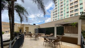 Un área de patio al aire libre con arreglos de asientos, una pared con vegetación y un edificio alto al fondo.