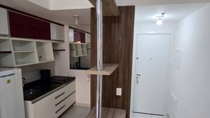 Una cocina moderna con armarios blancos, encimera negra y estufa integrada. Se observa un mueble de madera con puerta de vidrio y una puerta blanca al fondo.