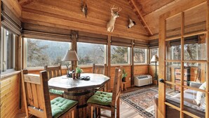 A wooden interior with a round dining table, wooden chairs, and a view of the outdoors through large windows.
