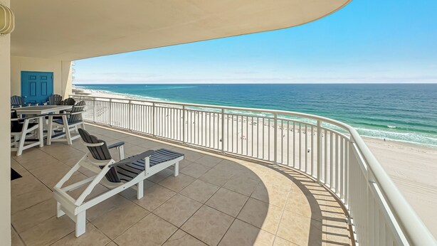 Uma varanda com vista para o oceano, uma mesa com cadeiras e uma porta azul.
