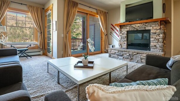 Un salon chaleureux avec une cheminée en pierre, un téléviseur à écran plat et une grande fenêtre agrémentée de rideaux.