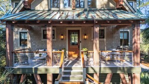 A two-story log cabin with a porch, wooden railings, and a front door. - Stunning Marsh Views! Plunge Pool, Quiet Kiawah 3BR Home! (Kiawah Island)