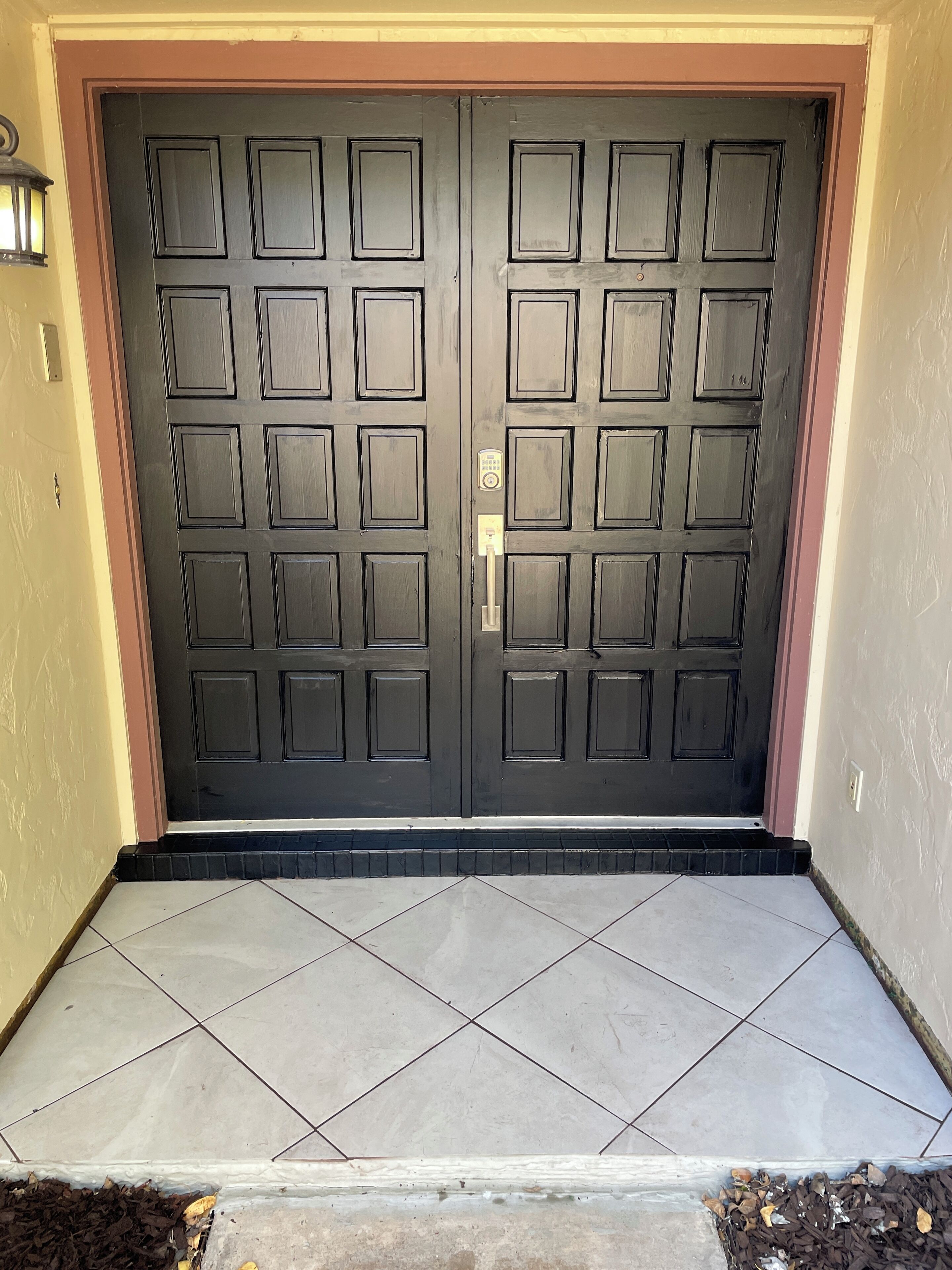 A double door with a keypad lock, set in a beige wall with a tiled entrance.