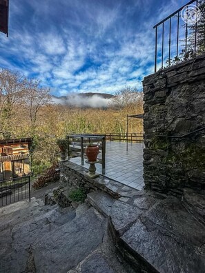 Een stenen trap die leidt naar een balkon met een balustrade, met uitzicht op een bergachtig landschap en een heldere lucht.