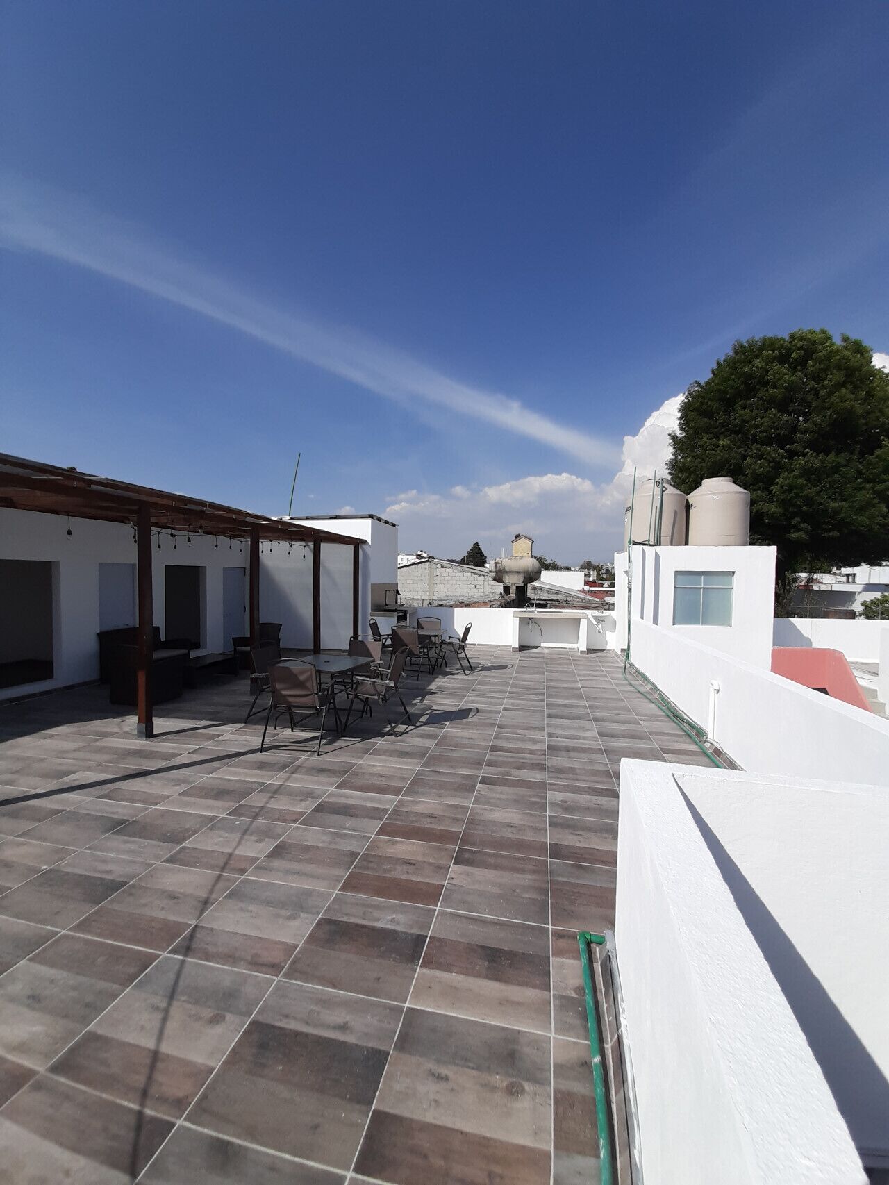 Eine Dachterrasse mit Sitzgelegenheiten im Freien, einer Pergola und Wassertanks.