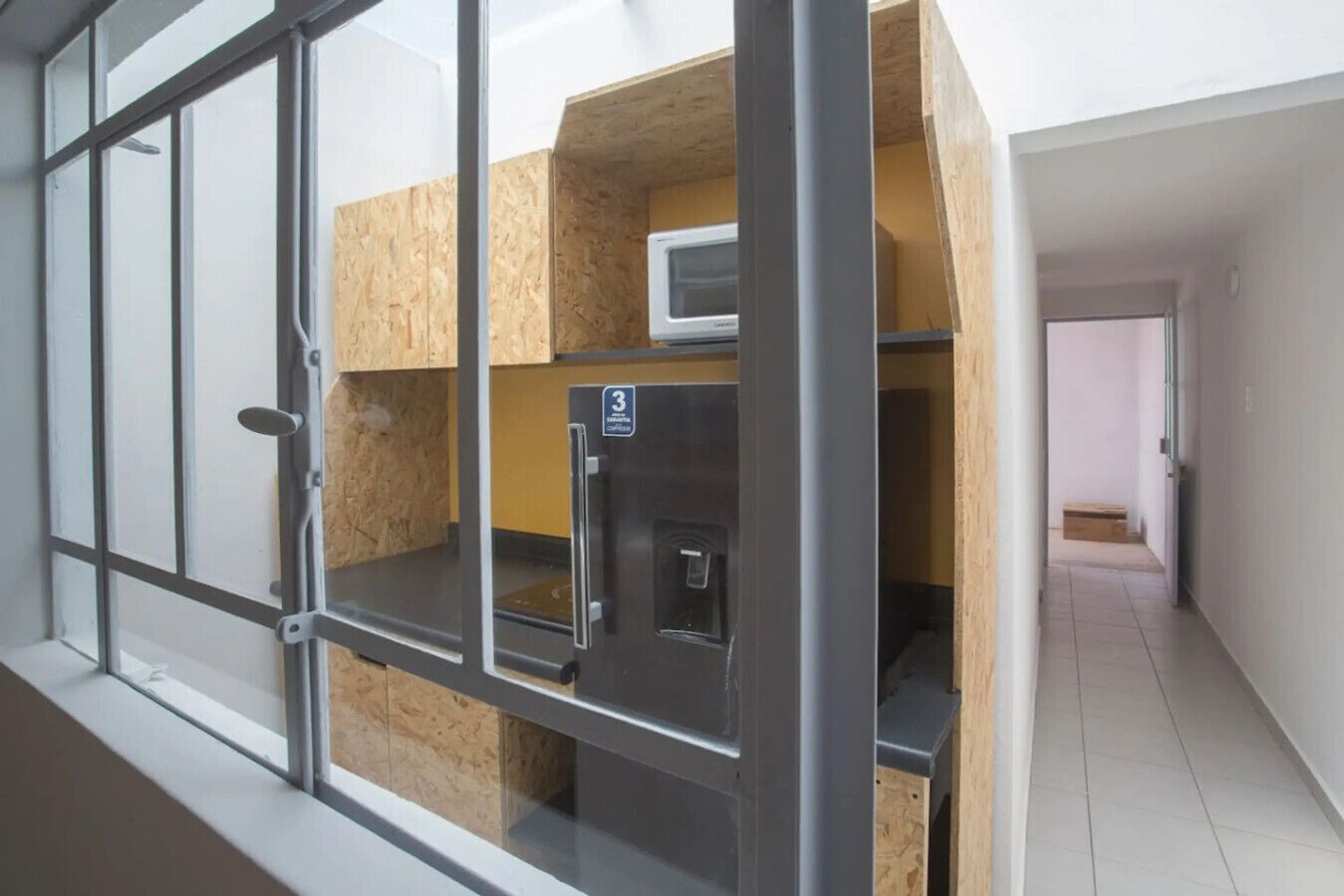 A room with a kitchenette, a window with metal bars, and a door leading to another room.