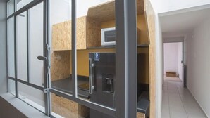 Une pièce avec un coin cuisine, une fenêtre avec des barreaux et une porte donnant sur une autre pièce.