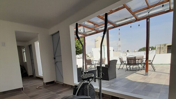 Une salle de sport moderne équipée d’un vélo d’exercice, d’un ventilateur de plafond et offrant une vue sur le paysage urbain grâce à de grandes fenêtres.