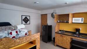 Ein kleines Hotelzimmer mit Bett, einer Küchenzeile, einem Kühlschrank und einer Mikrowelle.