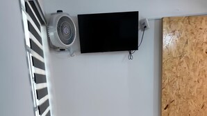 A small room with a black TV mounted on the wall, a black chair, a window with blinds, and a wooden door. - Depa cerca del Paseo Bravo (Puebla)