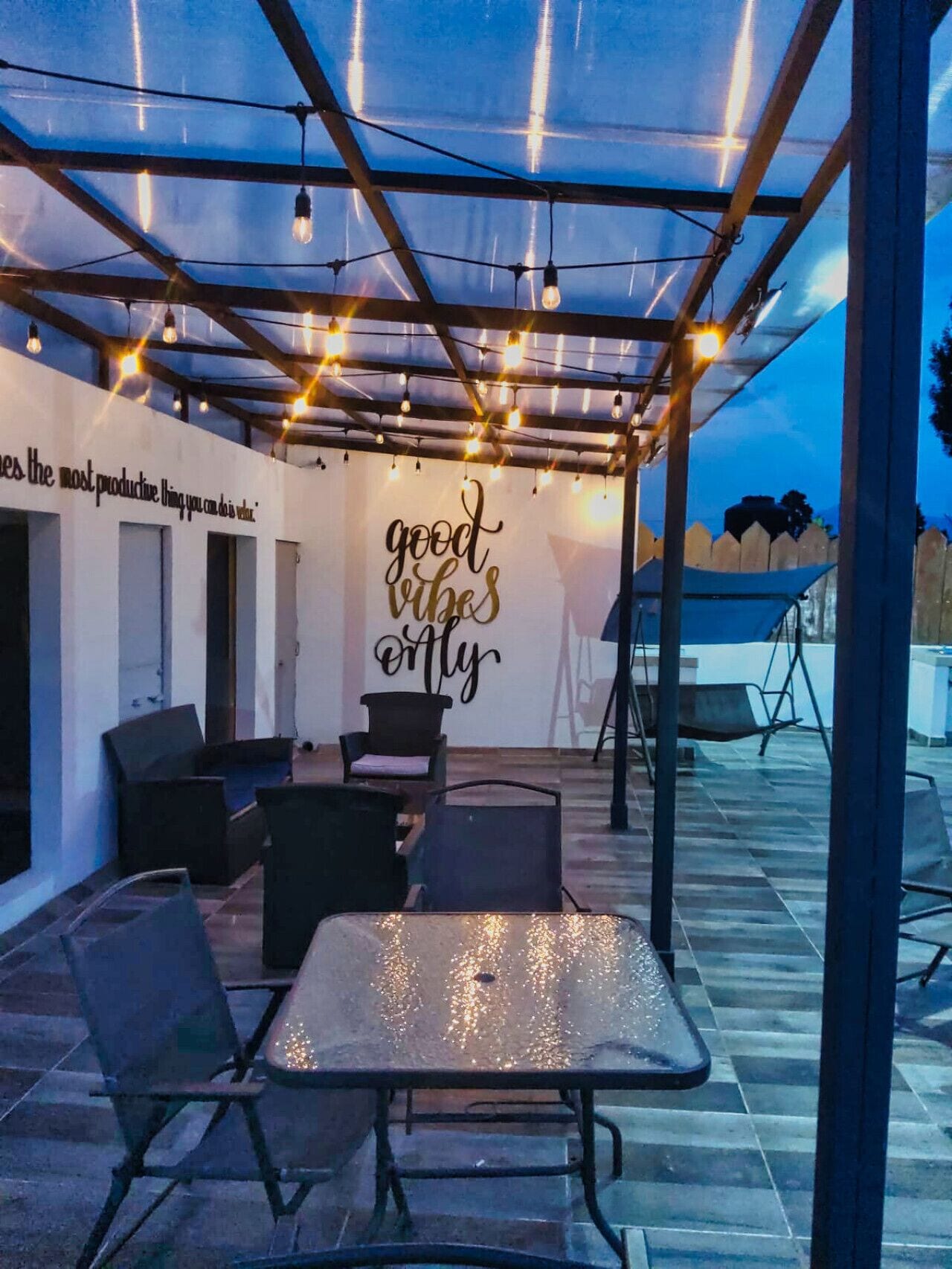 An outdoor patio with string lights, a table, chairs, and a wall with motivational writing.