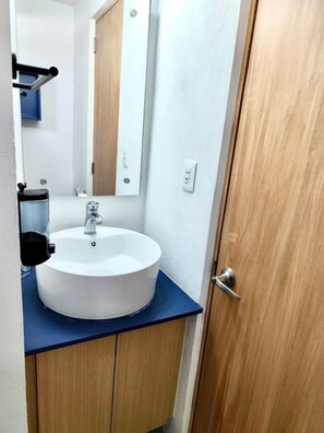 Une salle de bain avec un lavabo blanc, un miroir et une porte en bois.
