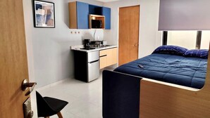Una camera compatta con un letto, angolo cottura e una porta che dà su un'altra stanza.