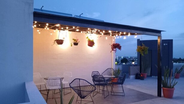 Una terrazza sul tetto con luci a tendina, piante in vaso e sedie moderne.