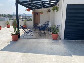 Une terrasse sur le toit, aménagée avec des espaces pour s’asseoir à l’extérieur, des plantes en pot et offrant une vue sur le paysage urbain.