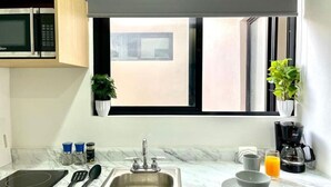 A kitchen with a sink, a microwave, a coffee maker, and a window with a view. - Smart loft with convertible bed/desk in Alameda (Santiago de Querétaro)