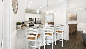 A modern kitchen with white cabinetry, a central island with bar stools, and pendant lighting. - Walk to Seaside, Beach! Private Pool & LSV! Sleeps 24, PETS OK! (Santa Rosa Beach)
