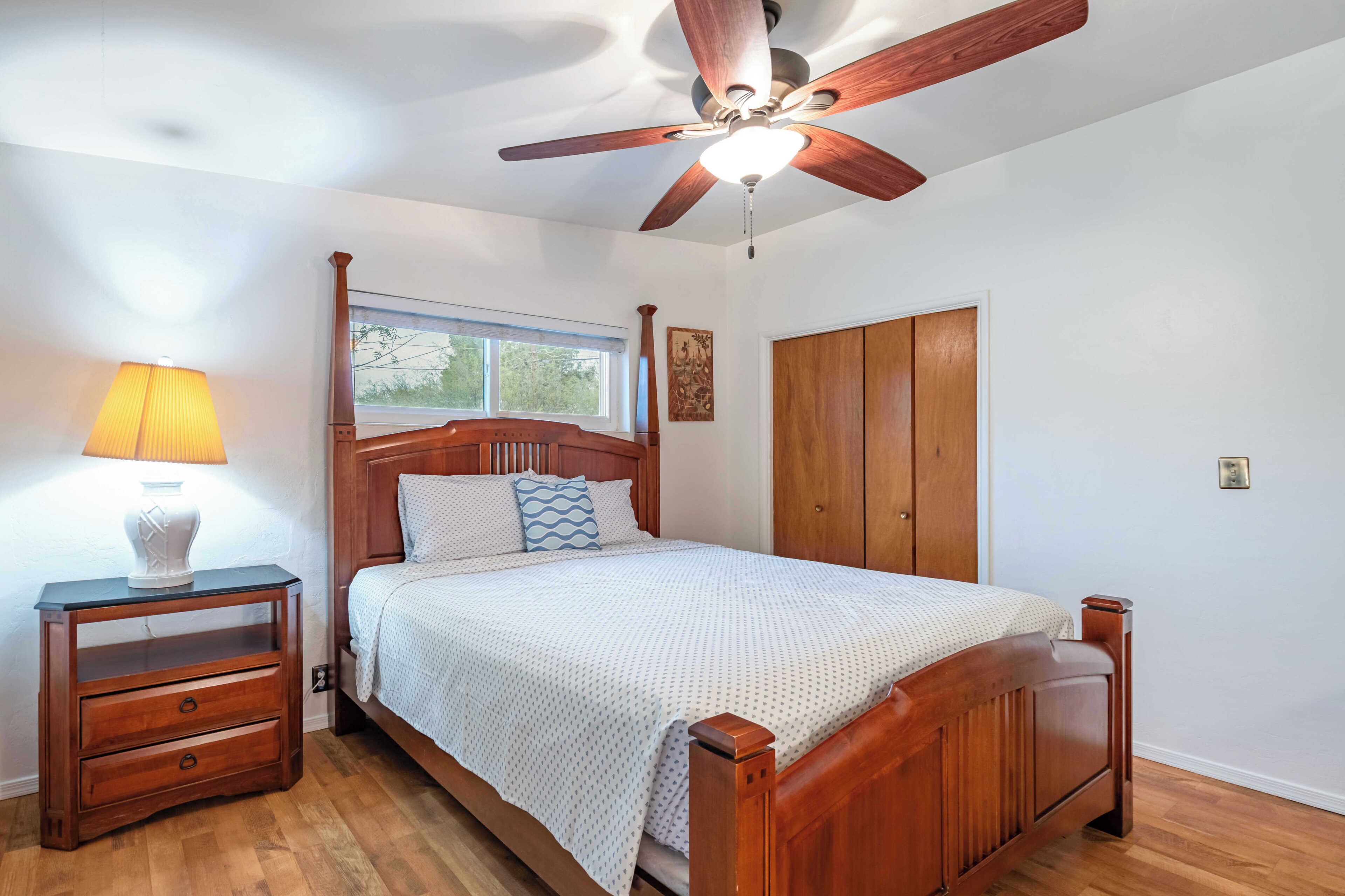 A bedroom with a wooden bed, a nightstand, a ceiling fan, a window, and a wardrobe.
