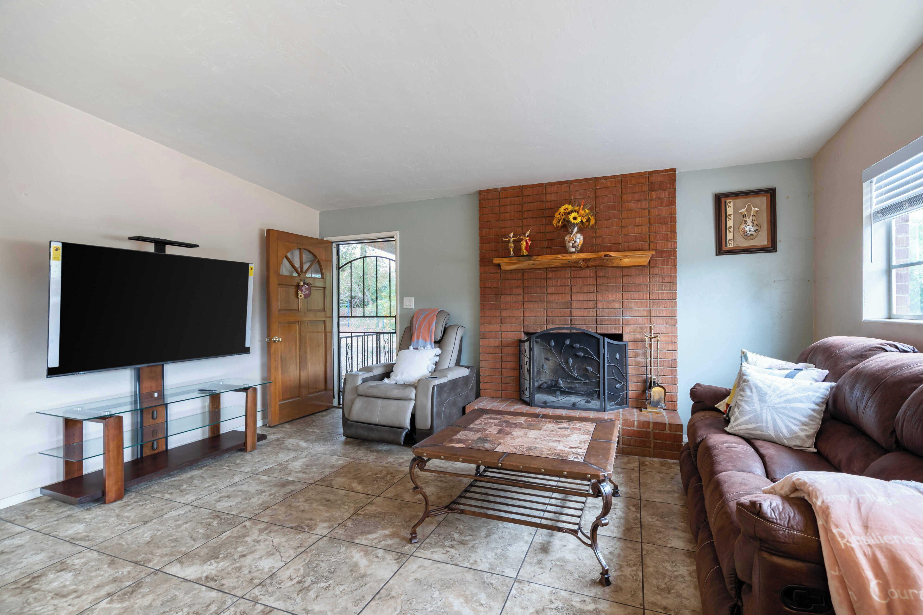 A living room with a flat-screen TV, a fireplace, a leather couch, and a glass coffee table.