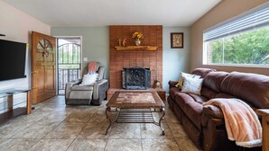 A living room with a fireplace, a sofa, a coffee table, and a television. - Central Tucson Gem w/ Porch, Patio & Park Access (Tucson)