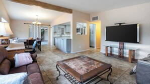 A living room with a sofa, a coffee table, a TV, and a kitchen in the background. - Central Tucson Gem w/ Porch, Patio & Park Access (Tucson)