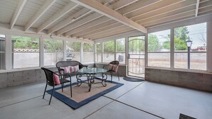 A covered patio area with a glass table and chairs, a brick wall, and large windows. - Central Tucson Gem w/ Porch, Patio & Park Access (Tucson)