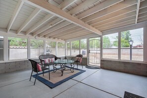 Ein überdachter Patio-Bereich mit einem Glastisch und Stühlen, einer Ziegelwand und großen Fenstern.