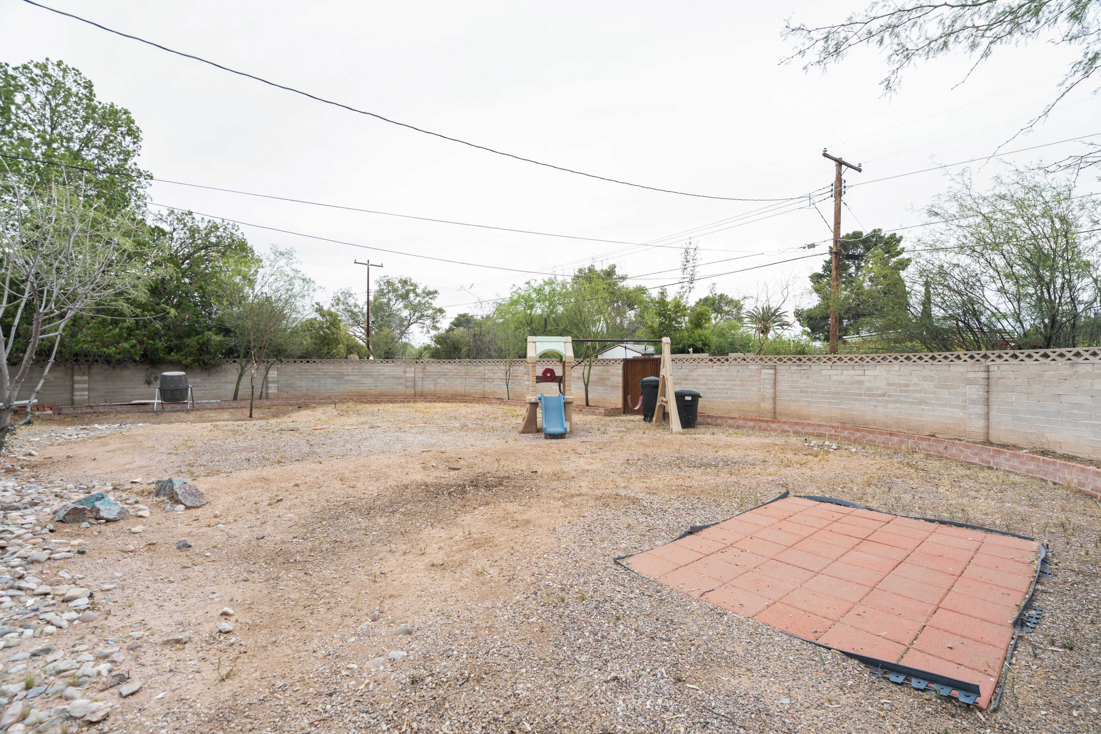 A backyard with a gravel area, a red rubber mat, a blue slide, and a brick wall.