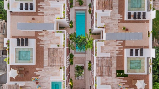Disposizione simmetrica dell'edificio con diverse piscine, zone relax all'aperto e vegetazione lussureggiante.