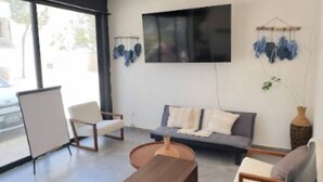Un soggiorno moderno con una scrivania di legno per la reception, un divano grigio e un televisore piatto montato a parete.