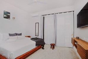 Une chambre à coucher avec un lit, une table de chevet, un miroir, une télévision et une fenêtre avec des rideaux.