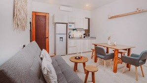 Ein gemütlicher Wohnbereich mit Sofa, Esstisch und Stühlen, einer kleinen Küchenzeile und einem Deckenventilator.