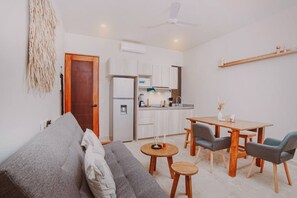 Ein gemütlicher Wohnbereich mit Sofa, Esstisch und Stühlen, einer kleinen Küchenzeile und einem Deckenventilator.