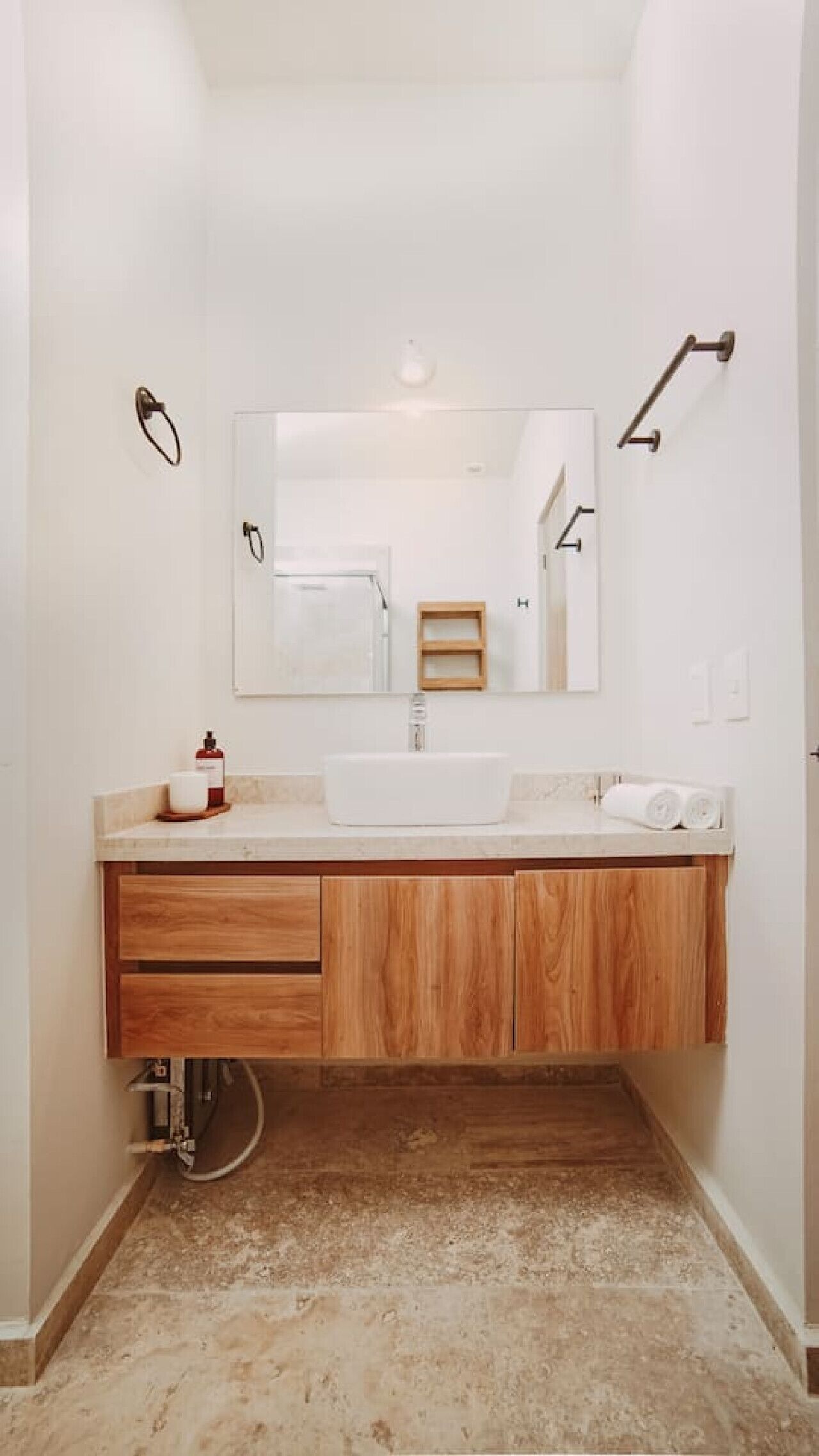 A bathroom with a white sink, wooden vanity, a mirror, and a towel rack.