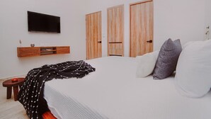 Ein Schlafzimmer mit einem Bett, einem an der Wand montierten Fernseher, Holzschränken und einem kleinen Tisch mit einer Kerze.