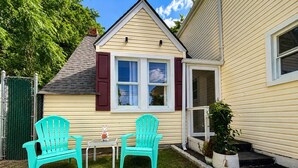 Et hus med en lille forhave, to turkise Adirondack-stole, et hvidt bord og en potteplante.