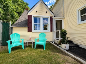 A house with a small front yard, two turquoise Adirondack chairs, a white table, and a potted plant.