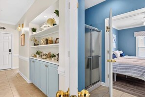 A room with a bed, a shower, and a white door. - Rising Tide by Brunswick Vacation Rentals: 4BR w/ Deck & Views, Near the Ocean! (Ocean Isle Beach)