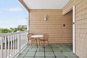 A balcony with a white railing, a round table with chairs, a lantern, and a beige wall. - Rising Tide by Brunswick Vacation Rentals: 4BR w/ Deck & Views, Near the Ocean! (Ocean Isle Beach)