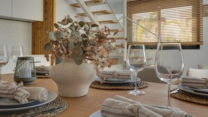 Ein Essbereich mit Holztisch, gedecktem Tisch für eine Mahlzeit, einer Blumenvase und einer Treppe im Hintergrund.