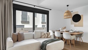 Ein modernes Wohnzimmer mit einer Eckcouch, Esstisch, Stühlen und einem großen Fenster mit Jalousien.