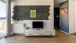 A modern living room with a stone wall, a flat-screen TV, a white console, and a window with curtains.